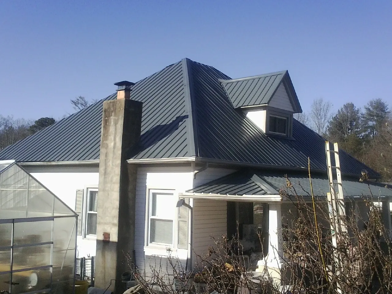 Dark blue standing seam metal roof on a white farmhouse with dormer — Slate & Tile Roof Repair by Roofing Brothers in Van Meter