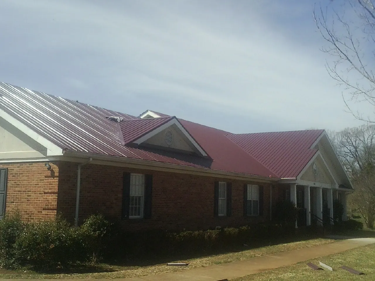 Red metal roof with gabled entries on a long brick building, from a Hail Damage Roof Repair job in Van Meter