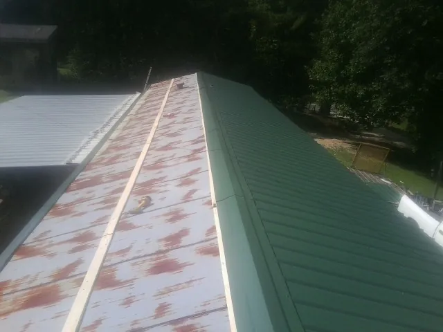 Old rusted panels beside newly installed green metal roofing — Wind Damage Roof Repair by Roofing Brothers in Van Meter