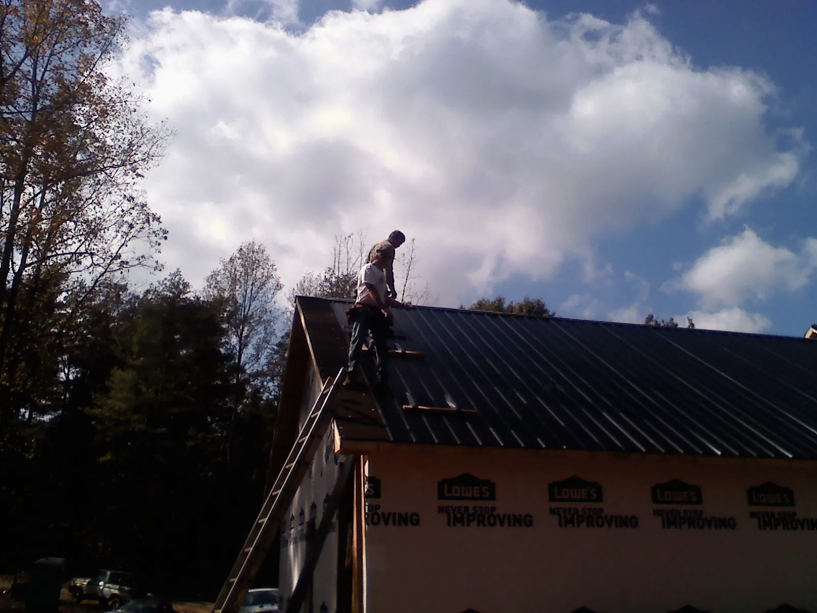 Roofer fastening dark metal panels high against a cloudy sky, from a Roof Inspection job in Van Meter