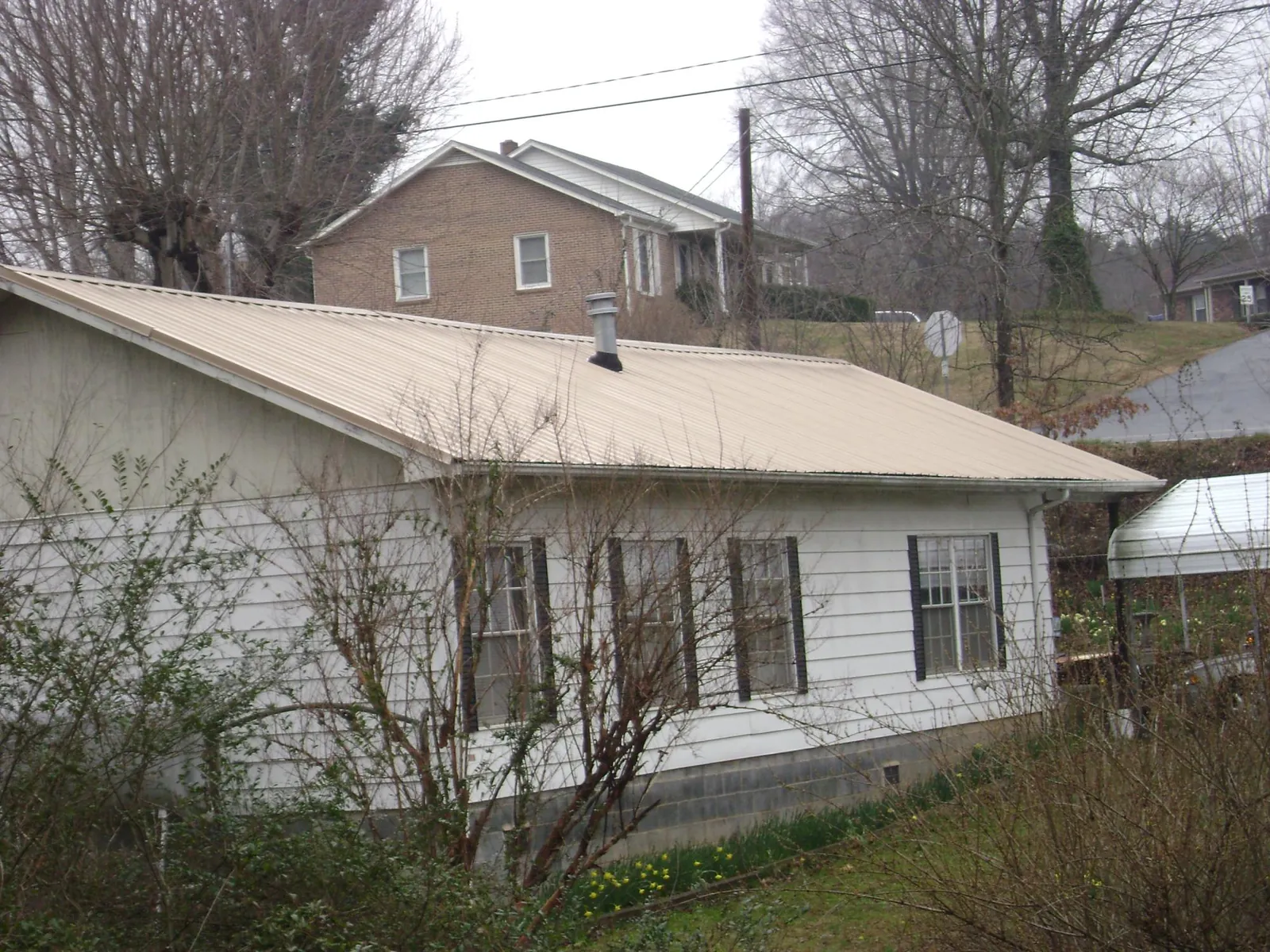 Tan metal roof on a white sided house set into a hillside — Commercial Roofing by Roofing Brothers in Van Meter
