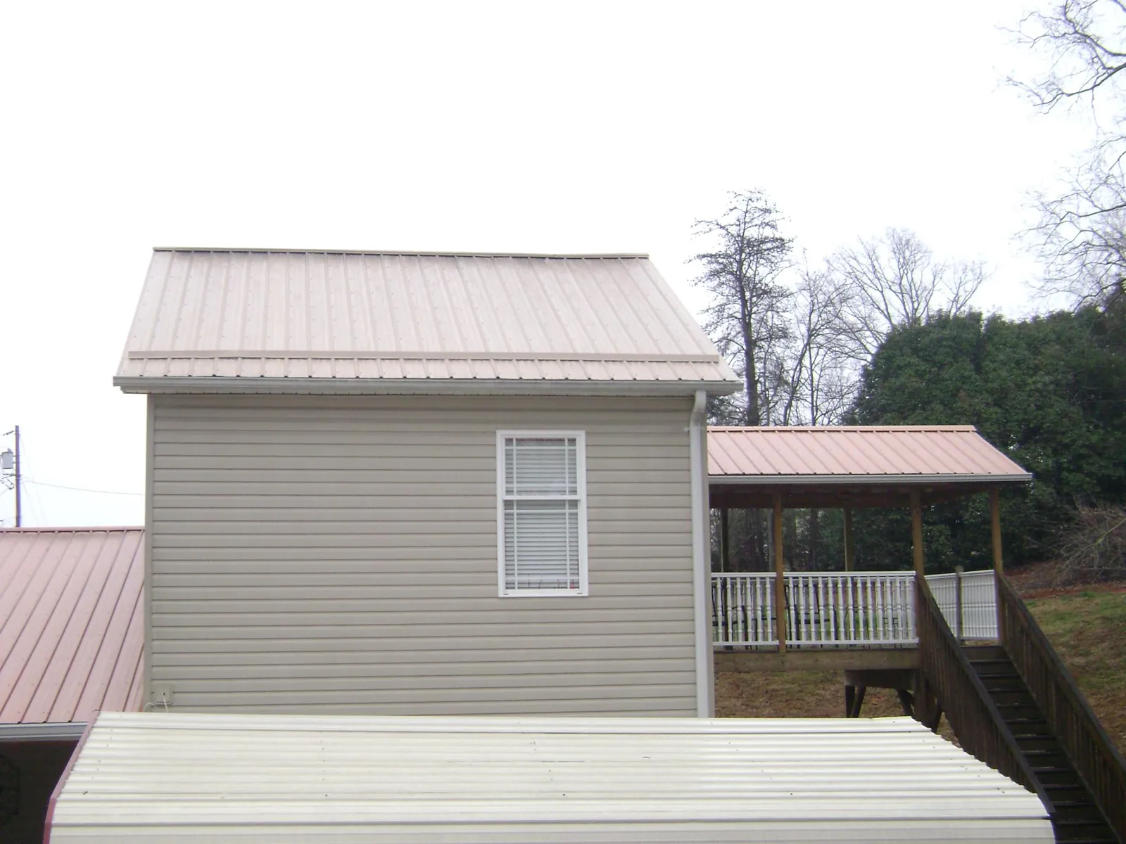 Tan metal roofs on a two story addition and attached porch, from a Roof Replacement job in Van Meter
